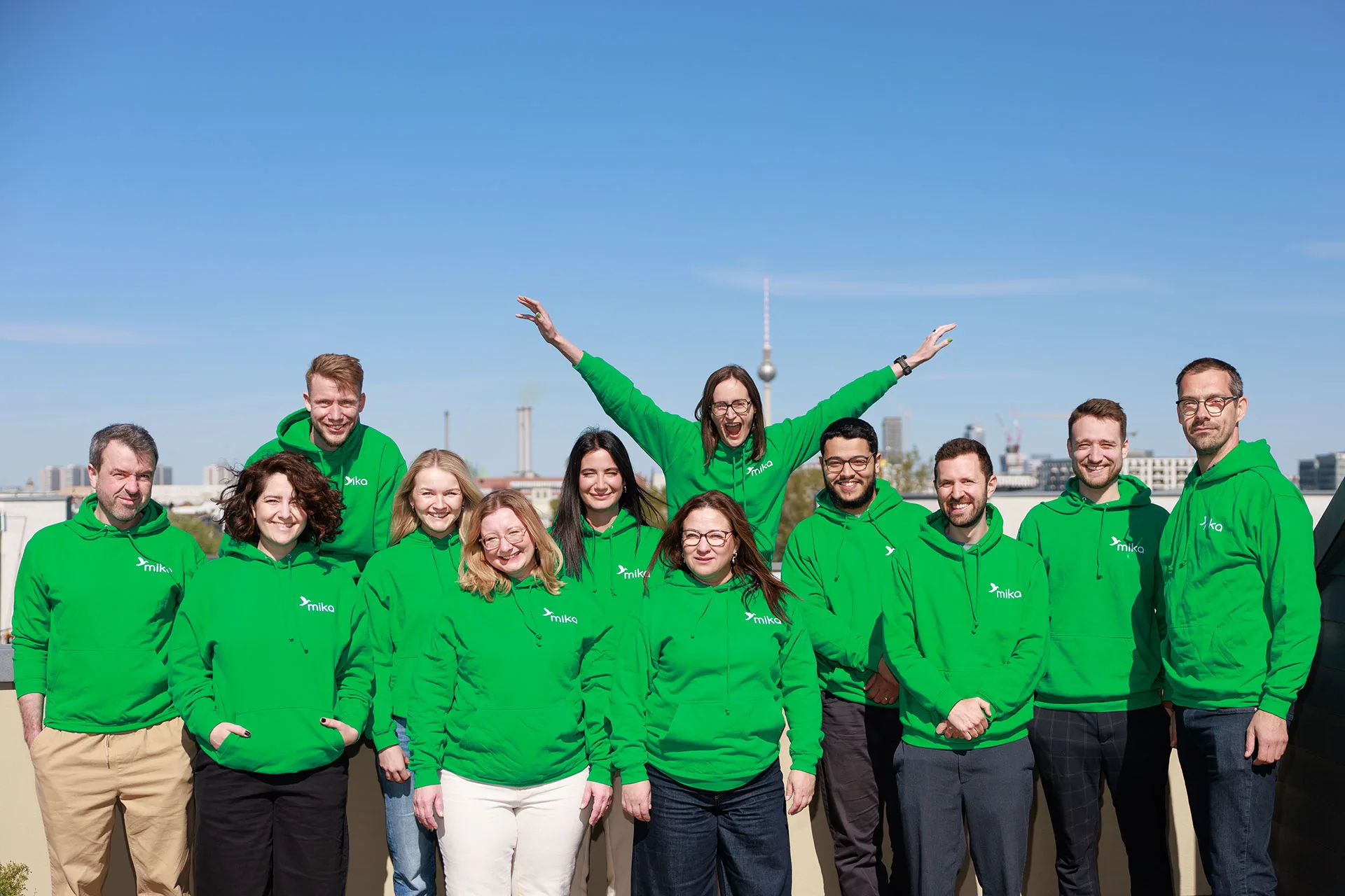 Das mika-Team in grünen Hoodies auf einer Dachterrasse in Berlin, im Hintergrund der Fernsehturm